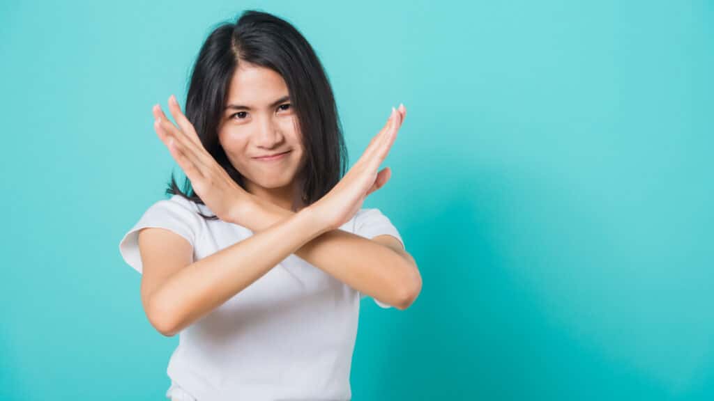 Portrait happy Asian beautiful young woman unhappy or confident standing wear white t-shirt, She holding two crossing arms say no X sign, studio shot on blue background with copy space for text
