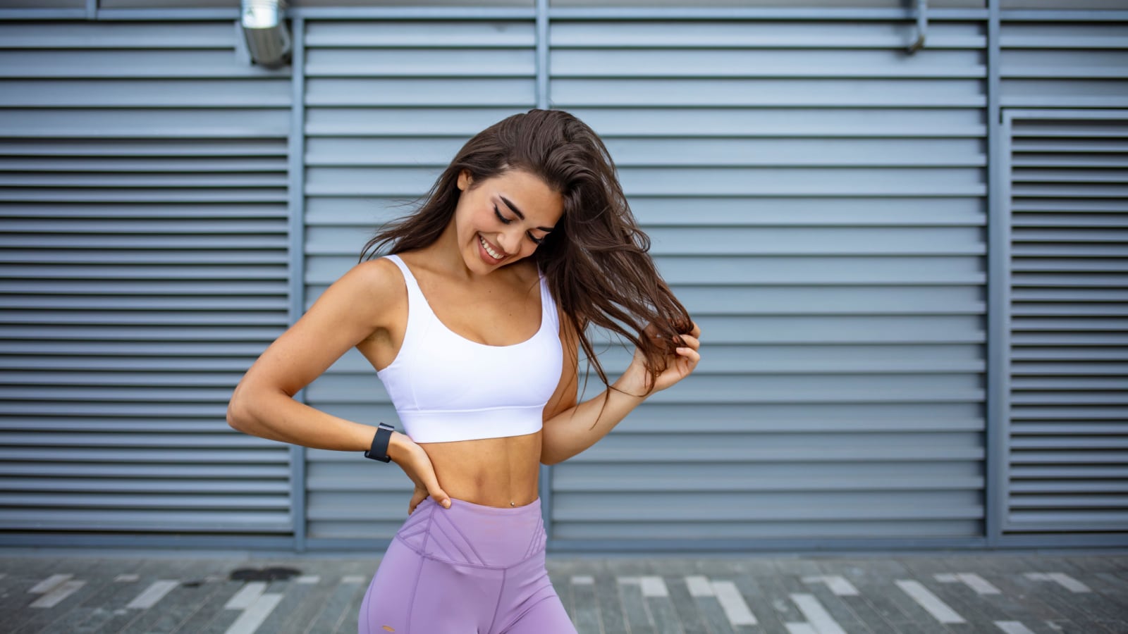 Slim young woman in sport outfit, happy, joyful, jumping. Happy young woman in sports clothing smiling. Muscular fitness model on black background looking away at copy space.