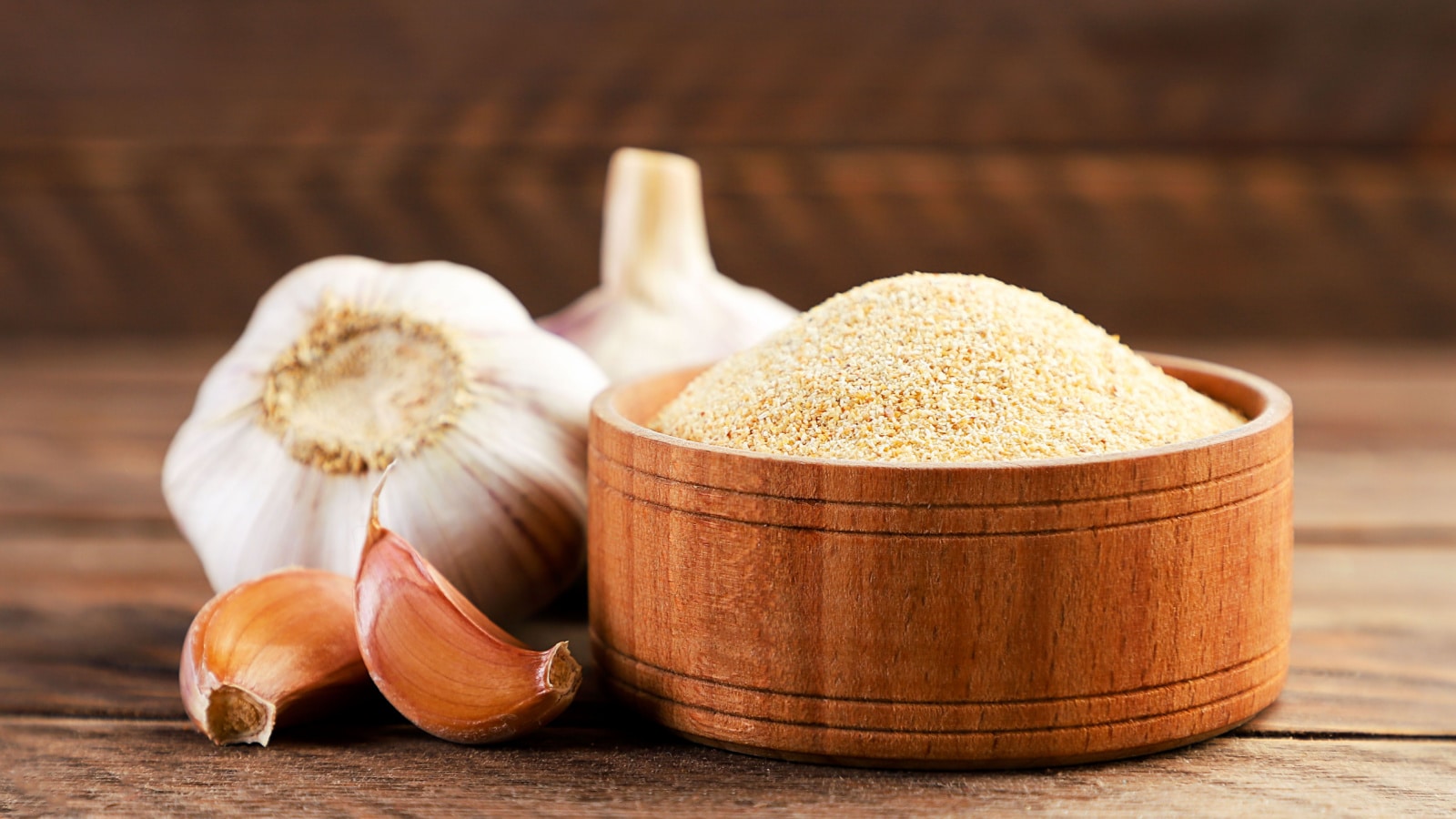 Ground garlic in a plate and cloves on a wooden background