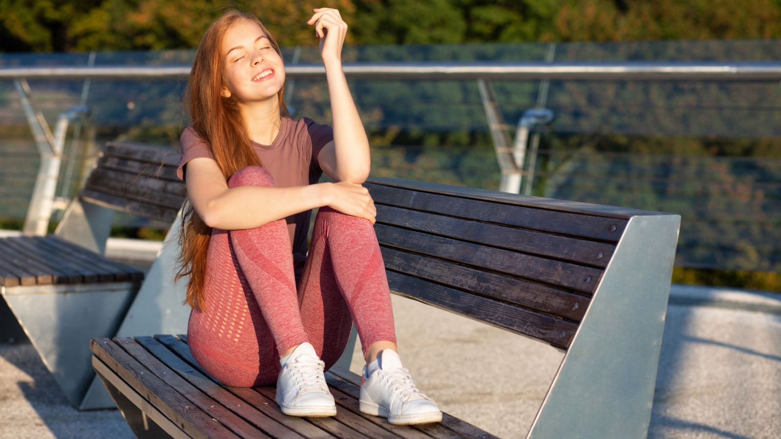 Young athletic red haired woman wears sport t shirt and leggins resting during workout outdoor. Empty space
