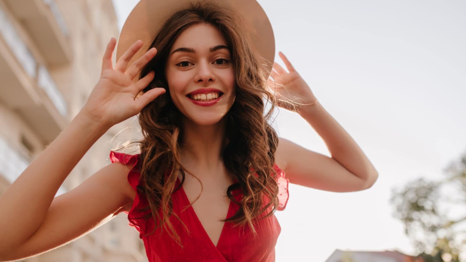 Close shot photography of cheerful girl touching her hat and beautiful long hair. Woman happy to be outside after the lockdown and enjoy the summer and warm weather in her favourite dress
