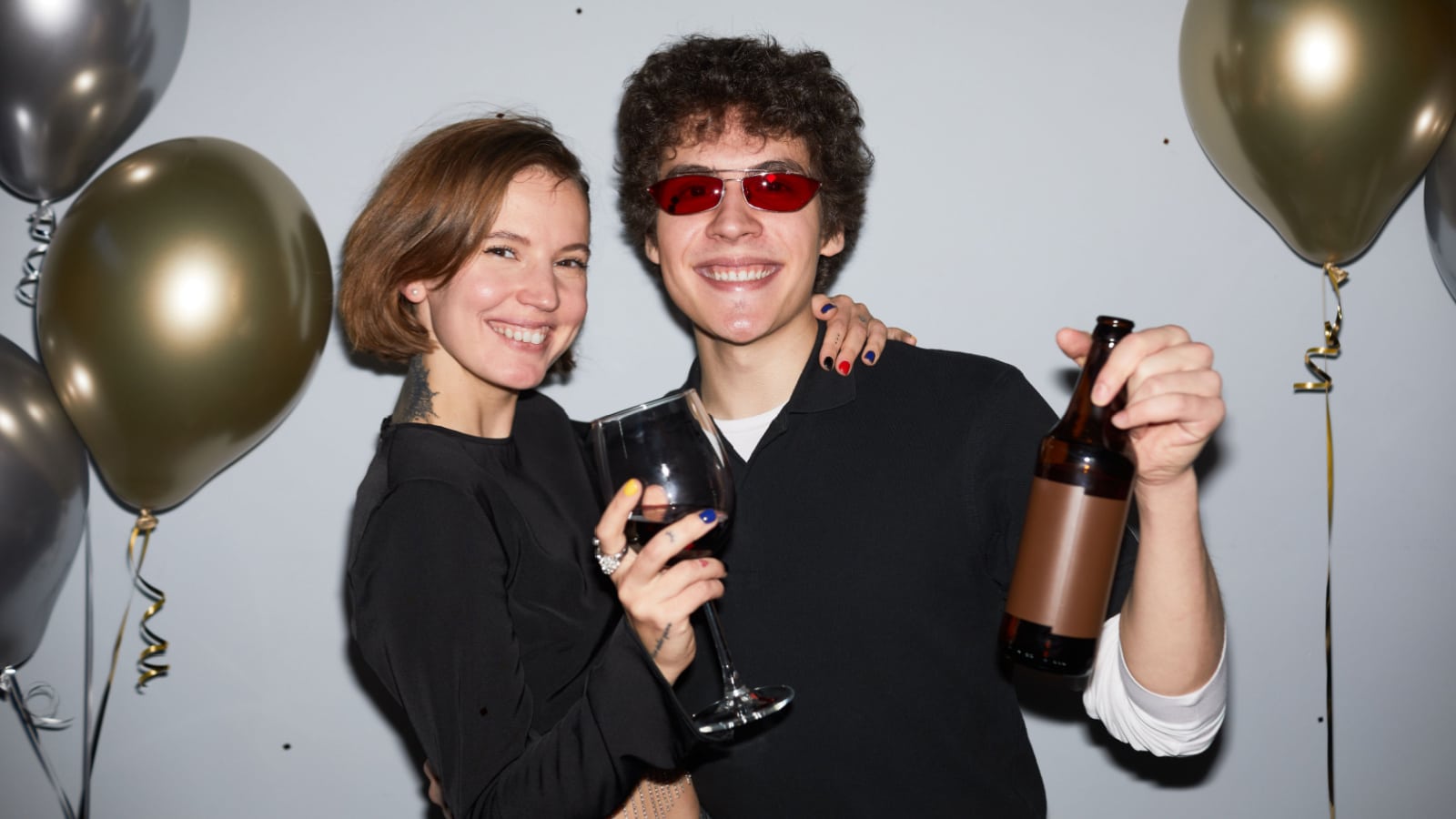 Waist up portrait of smiling young couple partying and looking at camera holding drinks, shot with flash