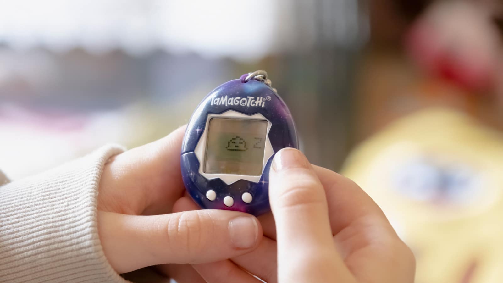 BARI, ITALY - MARCH 19, 2023: a kid playing with a Tamagotchi (portable handheld digital pet video game, created in Japan). Closeup of the creature sleeping.