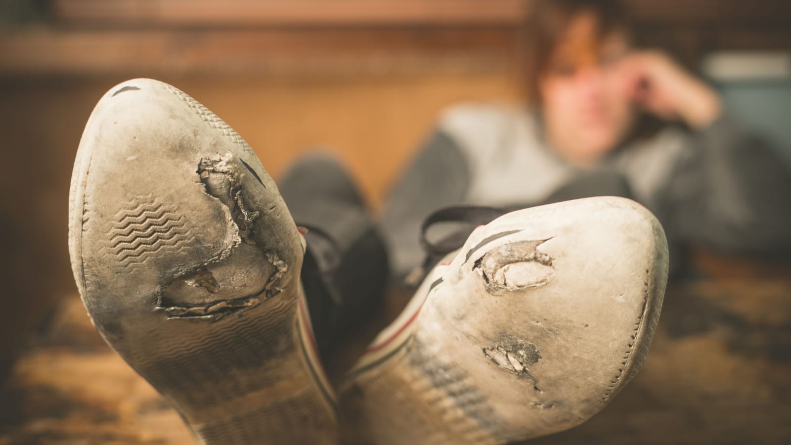 A young woman wearing worn out shoes is resting her feet on a table at home