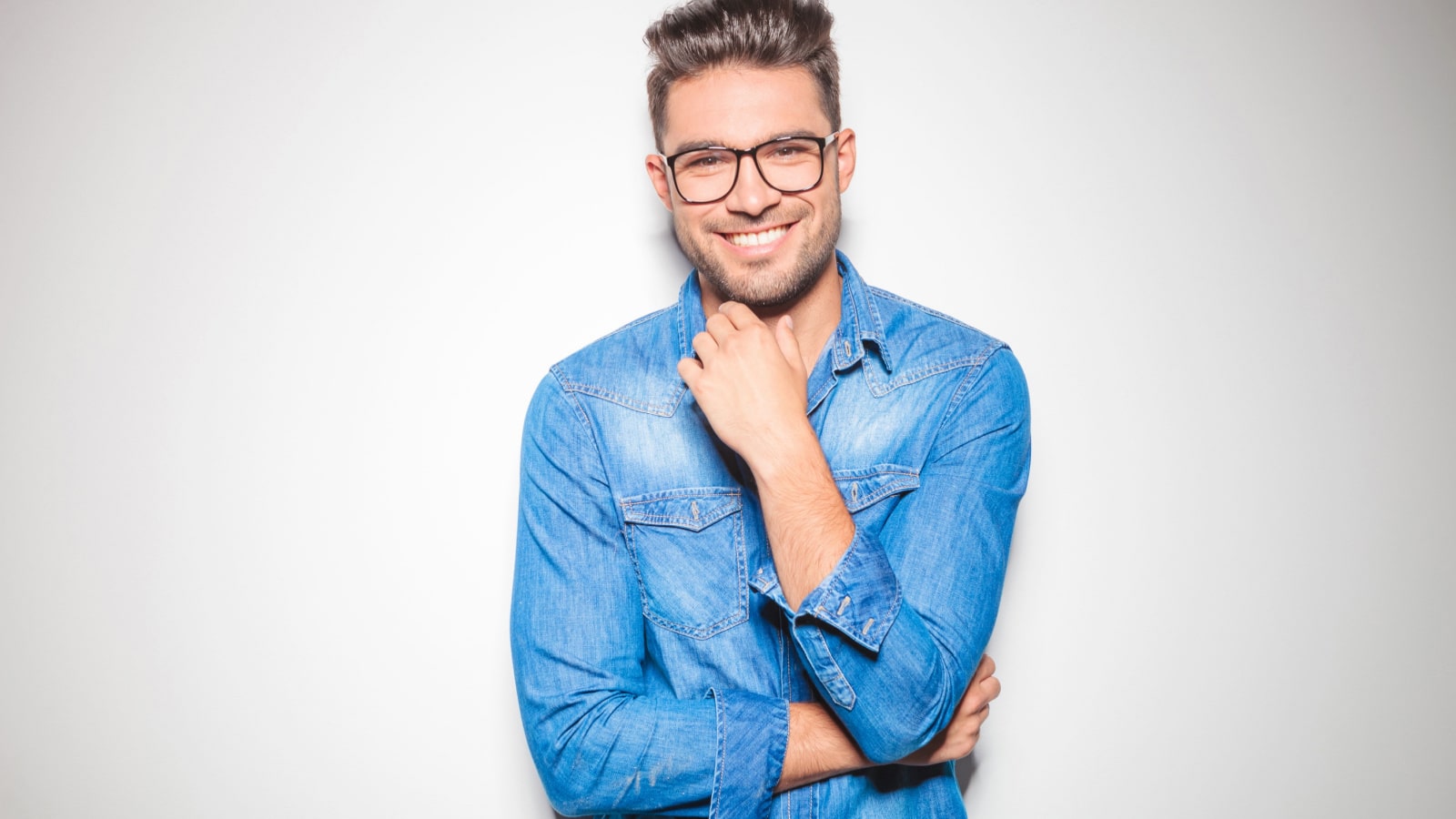 beautiful young man wearing glasses, smiling and touching his chin