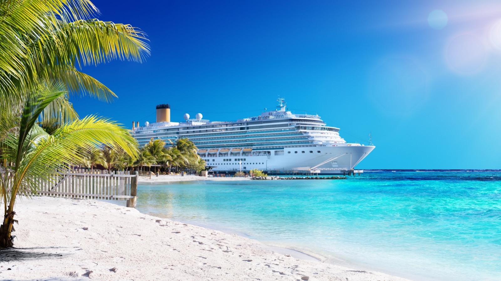 A cruise ship docs in the crystal clear waters of the Caribbean on a clear, sunny day.