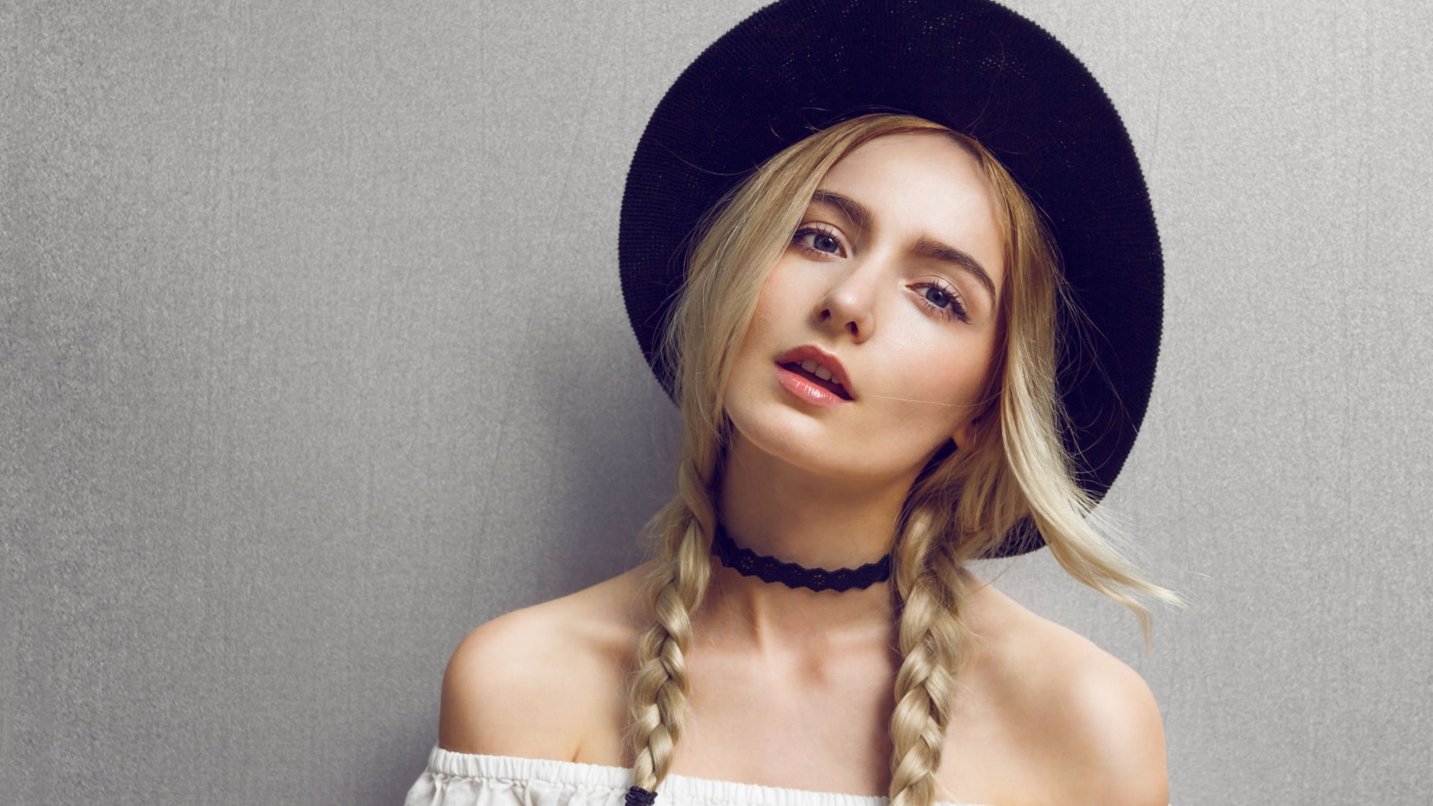 Pigtails. Close up of beautiful young blonde woman with black hat. Her hair is tied in two big ponytails. Around neck she has black choker. Professional make-up, hair style and styling.