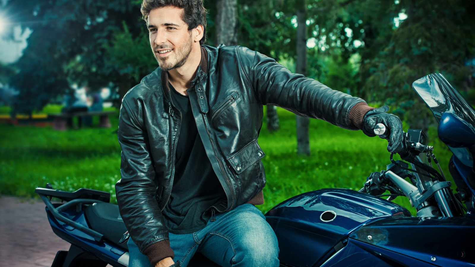 Sexy biker man wearing jeans and leather jacket sitting relaxed on his motorcycle.