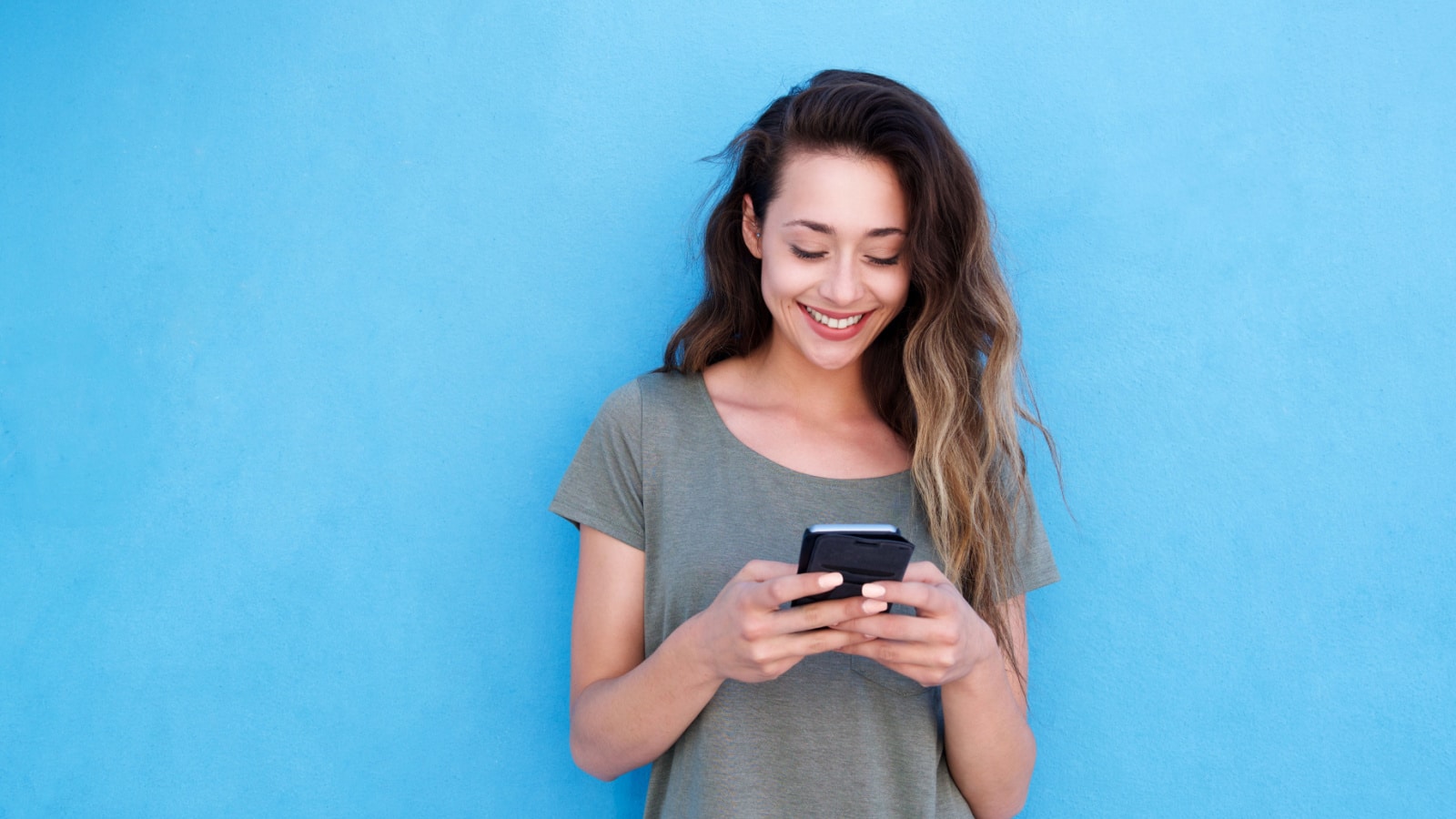 Front portrait of young smiling woman using mobile phone against blue background