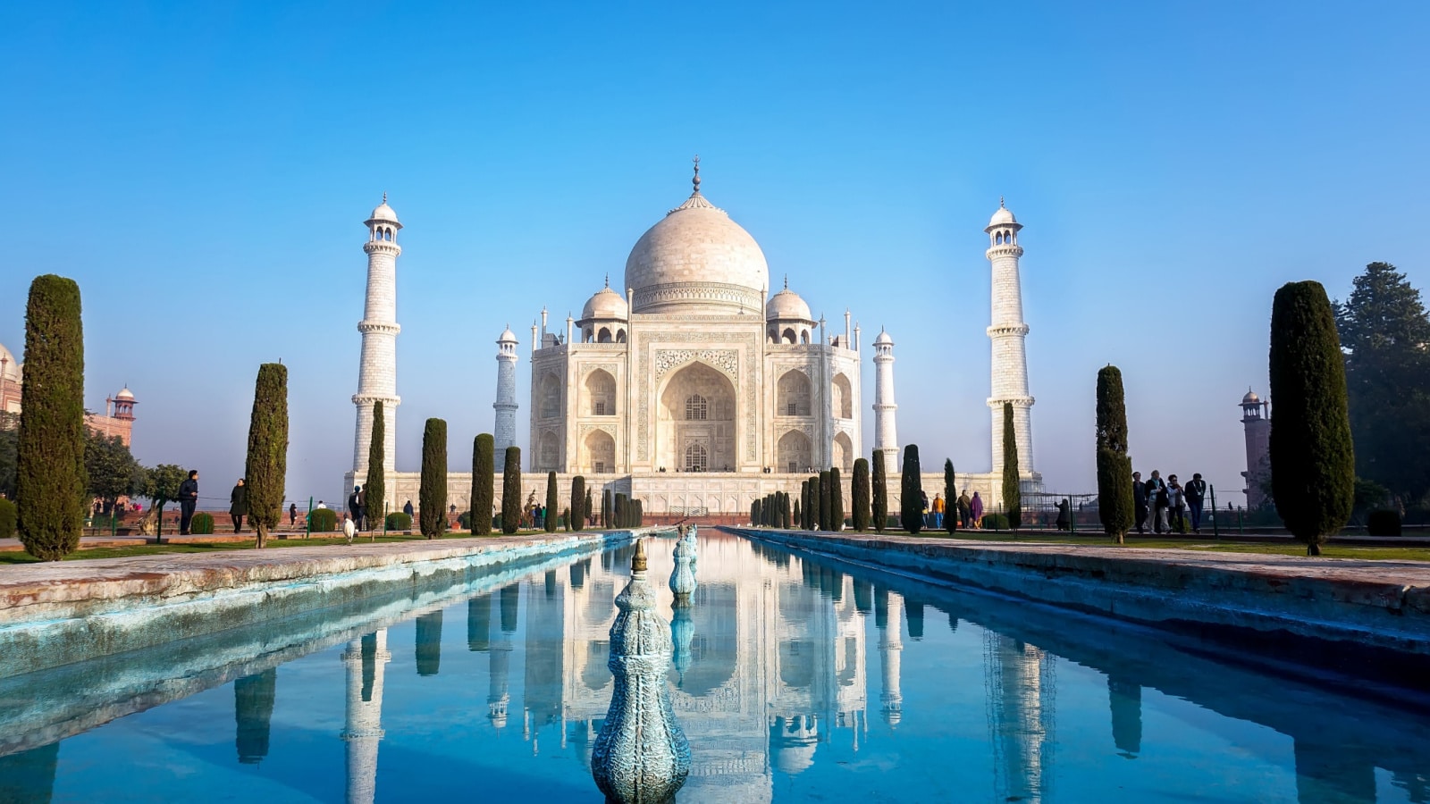 An iconic photo of the Taj Mahal monument reflecting off the waters of the garden pools on a clear morning in Agra, India.