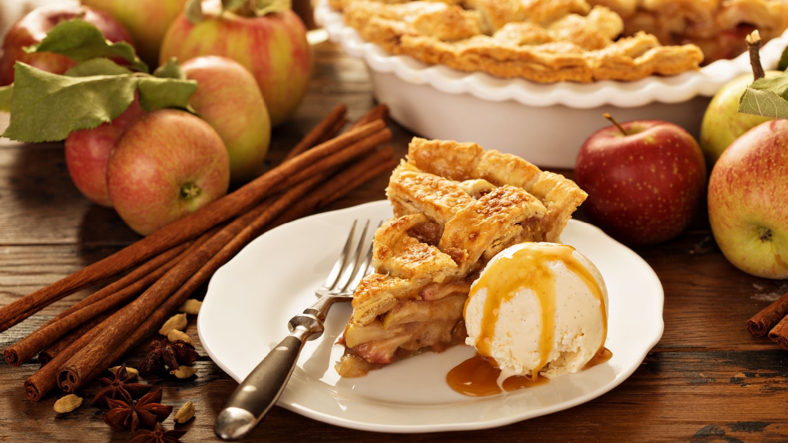 Piece of an apple pie with ice cream scoop and caramel sauce on a plate, fall baking concept