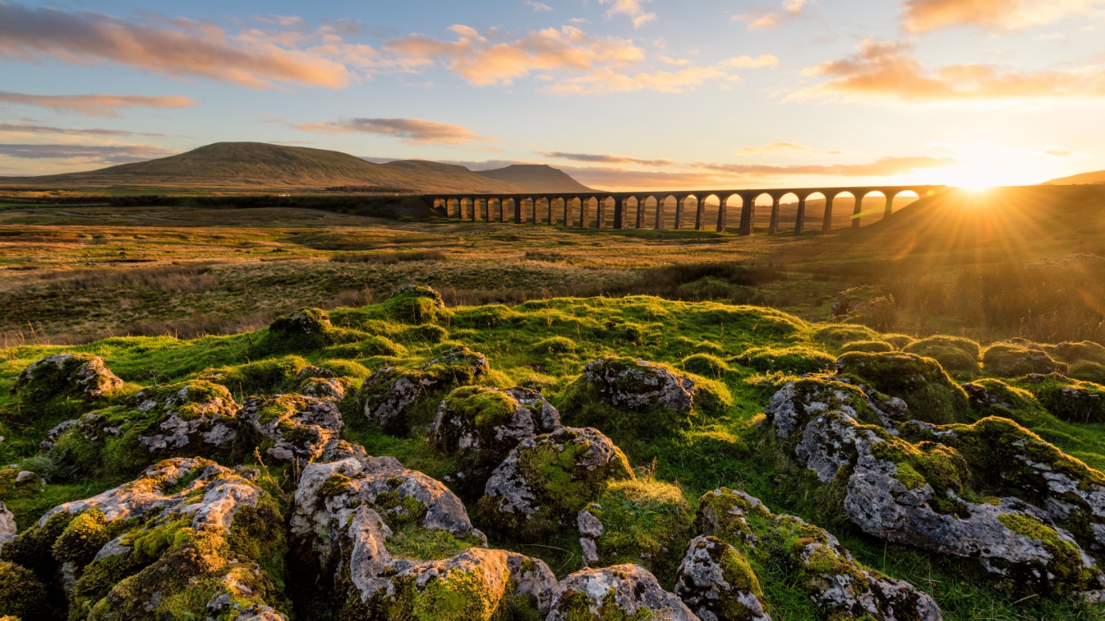 Gorgeous golden light as the sun sets behind the Ribblehead Viaduct with rocks in foreground. Yorkshire Dales