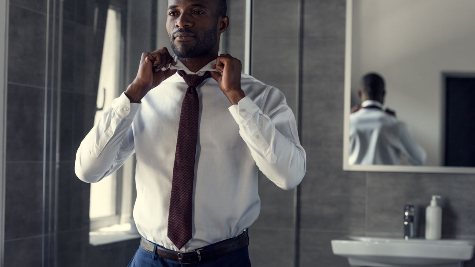 happy young businessman in white shirt putting on his tie at bathroom