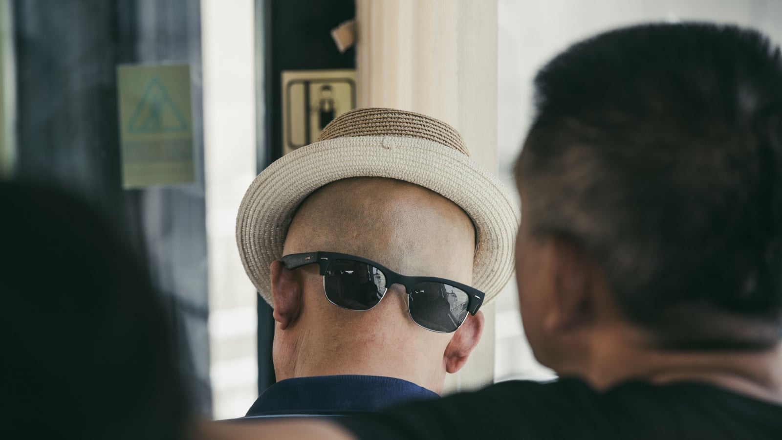 Xian, China - July 2019 : A chinese man wearing his sunglasses on the back of his shaved head with a hat that gives the illusion of a face, public transport