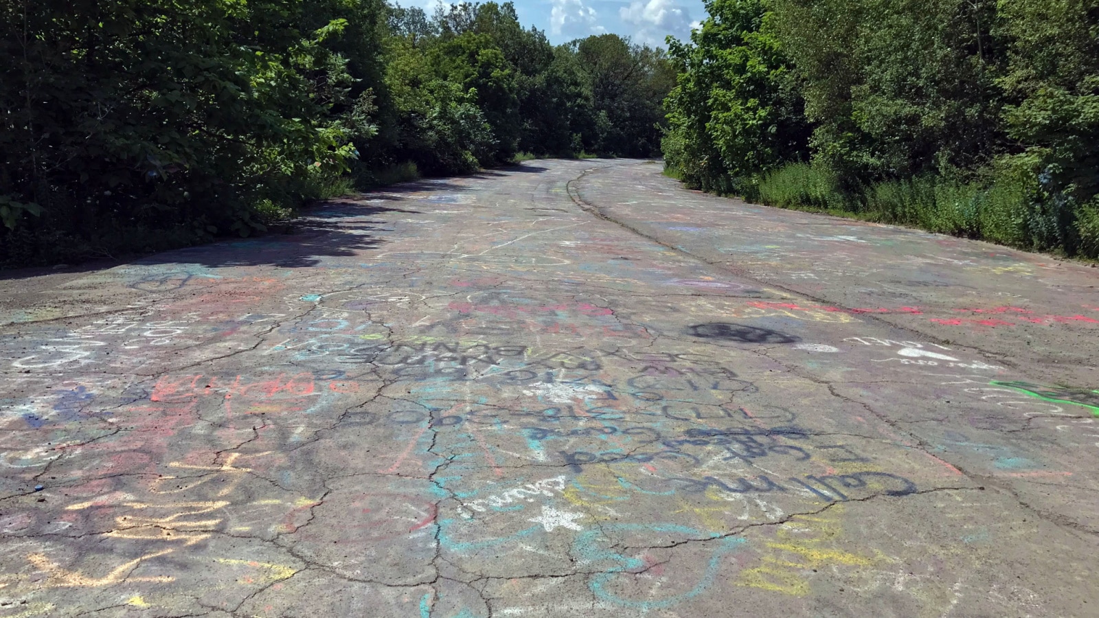 An abandoned highway road in Centralia, Pennsylvania, filled with graffiti and lush trees and woods lining either side of the road.