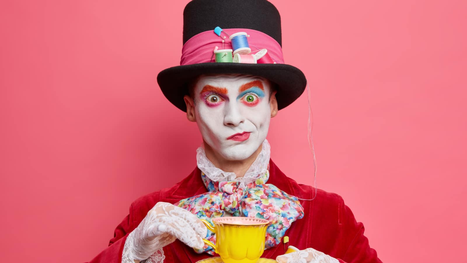 Horizontal shot of serious male hatter poses with cup of tea wears hat has manners of aristocratic gentleman dresses for masquerade carnival poses indoor. Halloween and entertainment concept