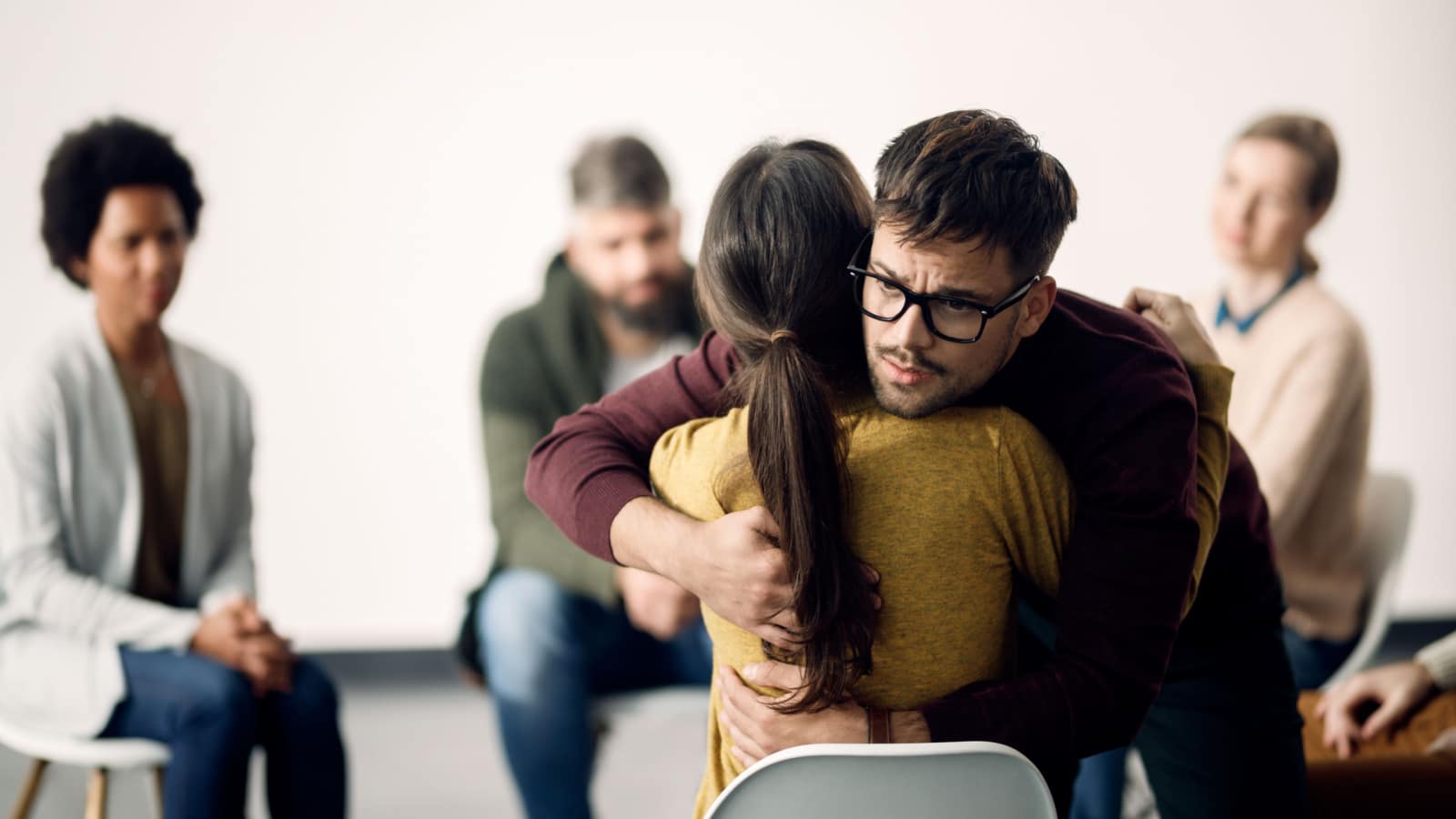 Young sad man hugging female participant of group therapy during the meeting.