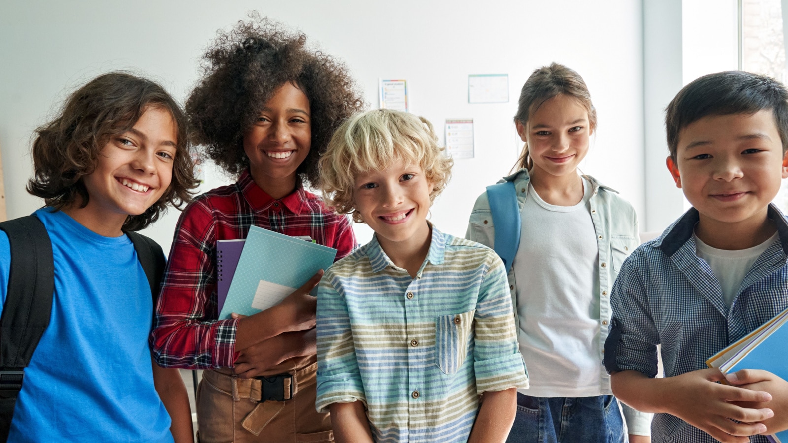 Happy diverse junior school students children group looking at camera standing in classroom. Smiling multiethnic cool kids boys and girls friends posing for group portrait together.