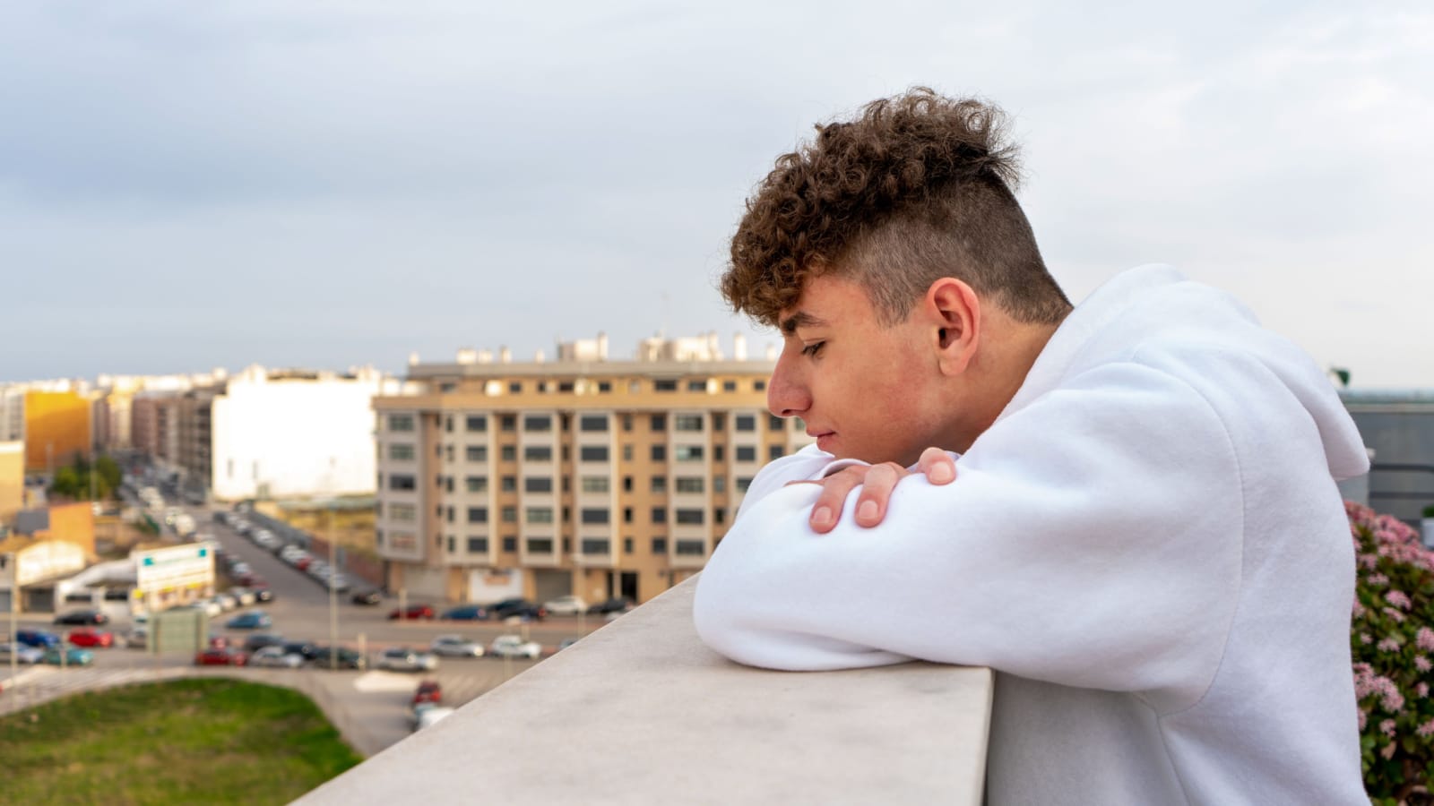 Young Caucasian man with curly hair dressed in a white sweatshirt looking at the city skyline serious and melancholic, I think about his future and what life has prepared for him broccoli hair