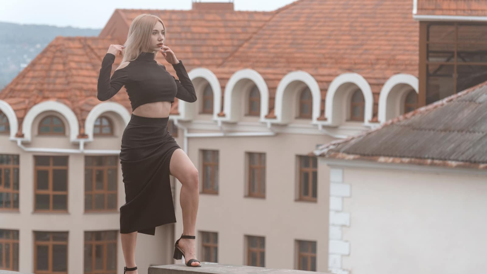 Stylish woman in black outfit and heels.Young sexy model poses for photo on ancient architecture background.