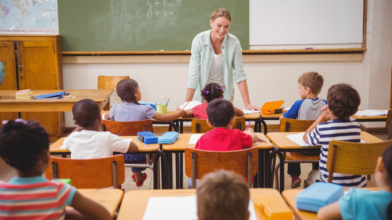 Pretty teacher talking to the young pupils in classroom at the elementary school