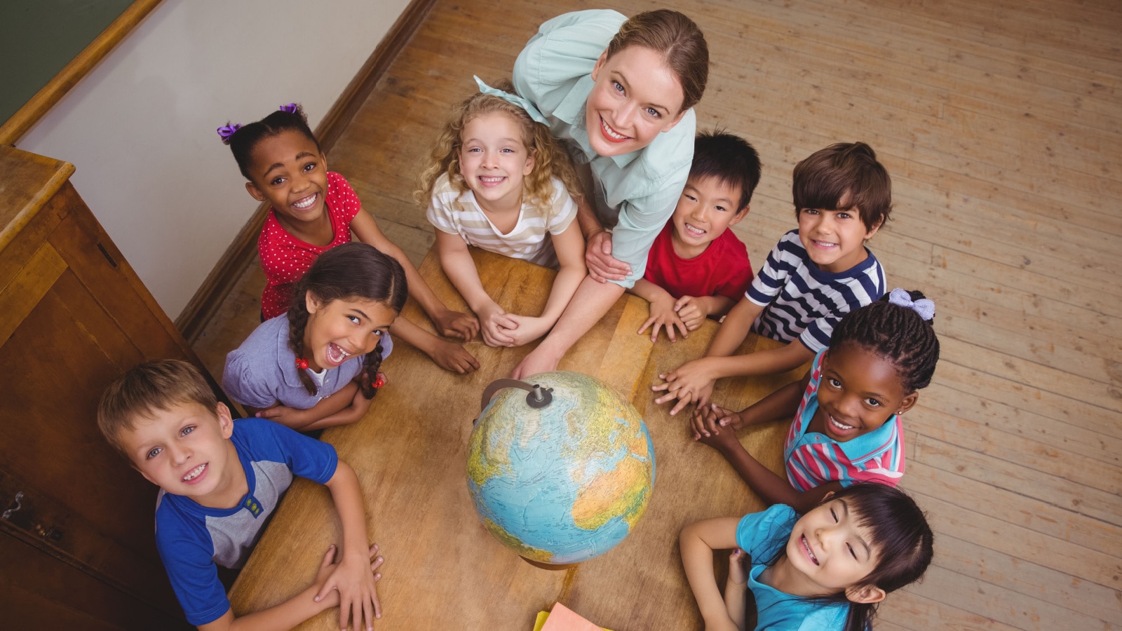 Cute pupils smiling around a globe in classroom with teacher at the elementary school