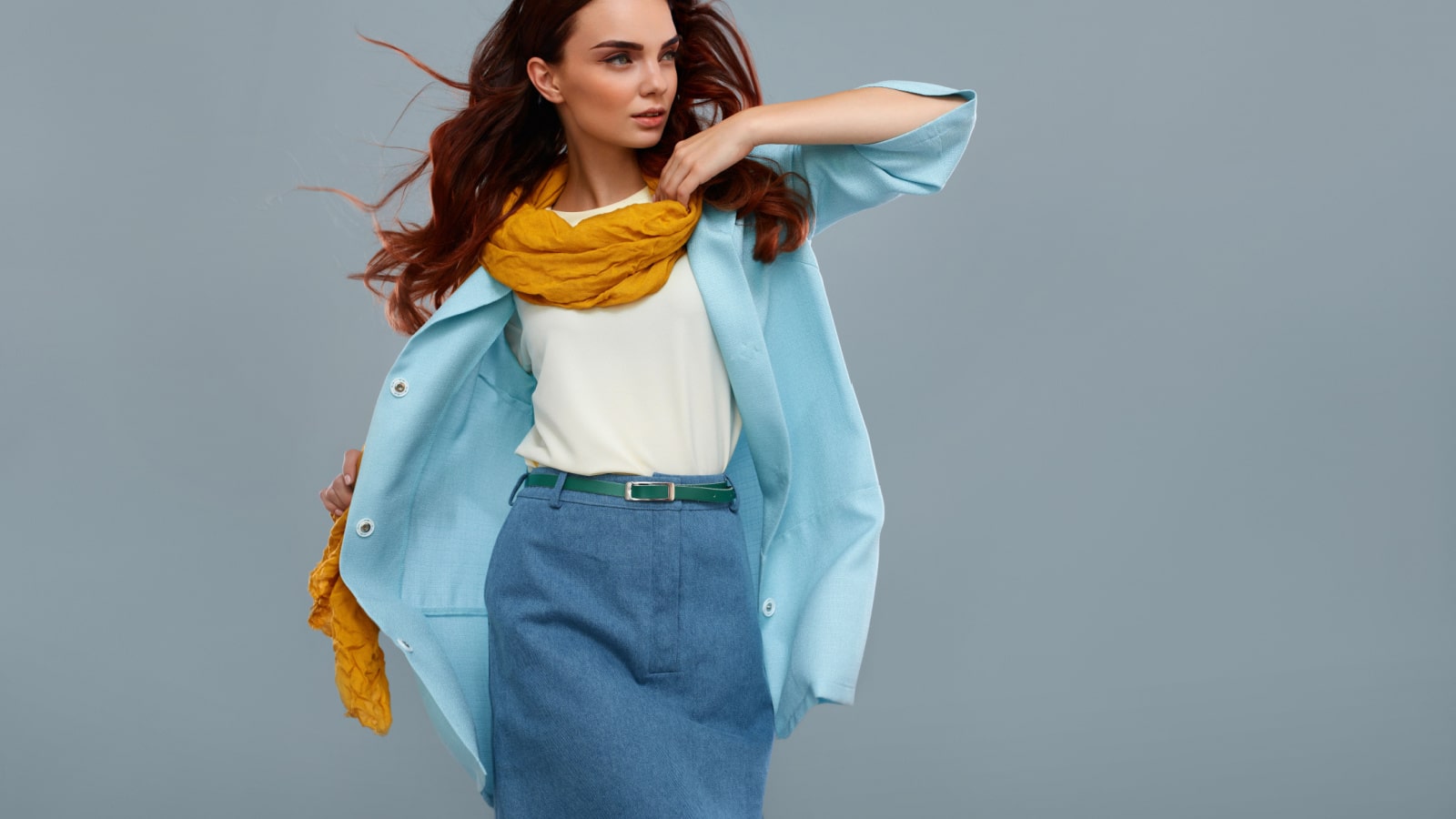 Fashion Model Girl In Fashionable Clothes On Grey Background. Beautiful Sexy Woman Wearing Stylish Clothing, White Shirt, Jeans Skirt, Light Blue Coat Jacket, Yellow Scarf In Studio. High Resolution