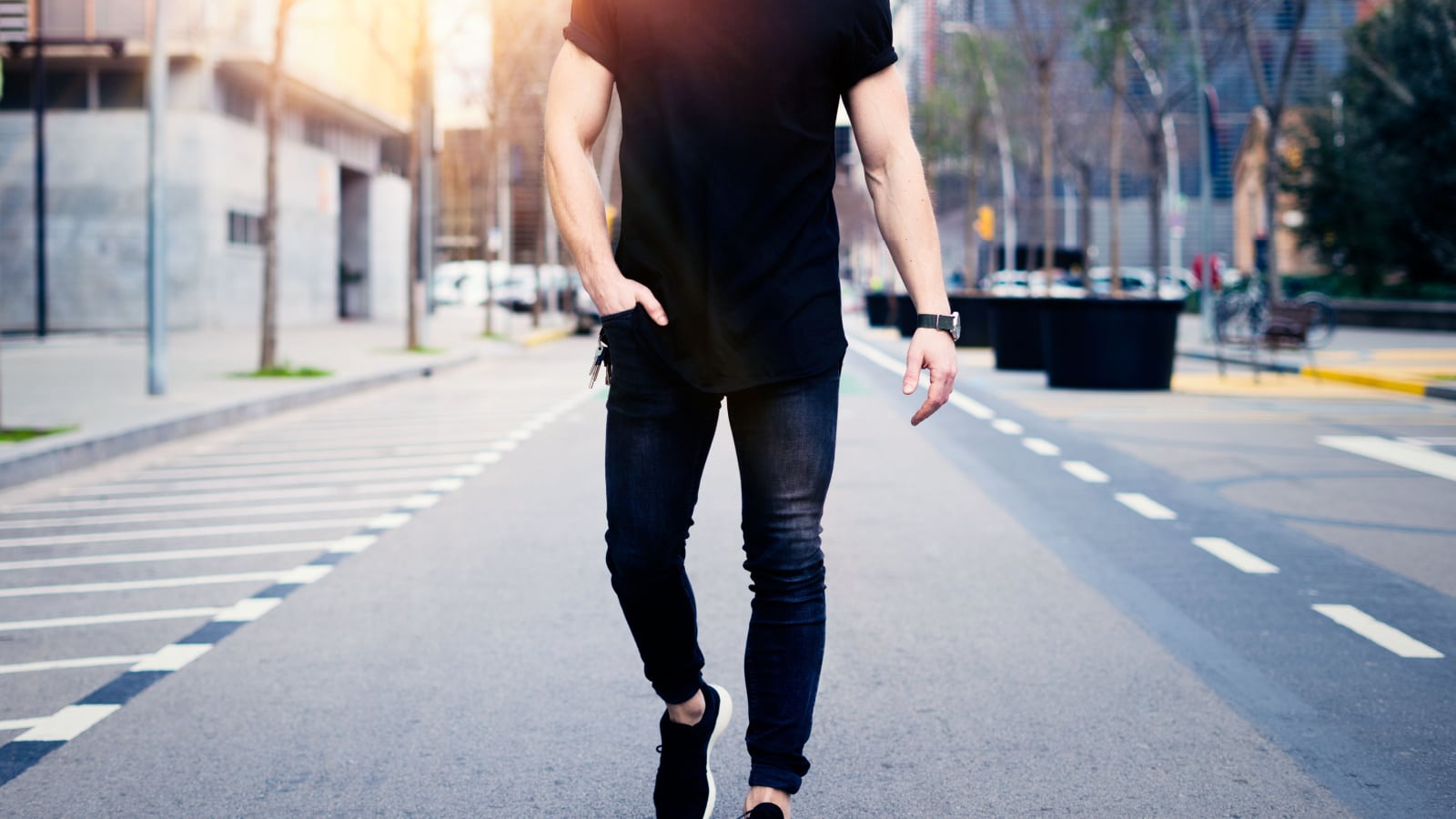 Young muscular man wearing black tshirt and jeans walking on the streets of the modern city. Blurred background. Hotizontal mockup