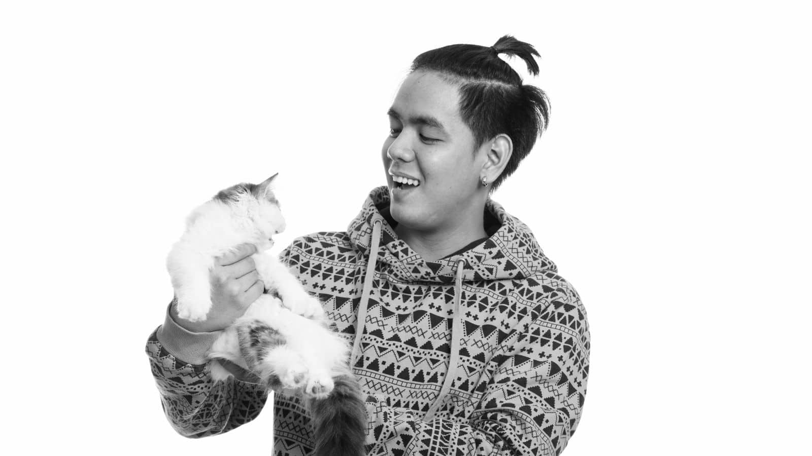 Studio shot of young happy Asian man smiling while holding cute cat