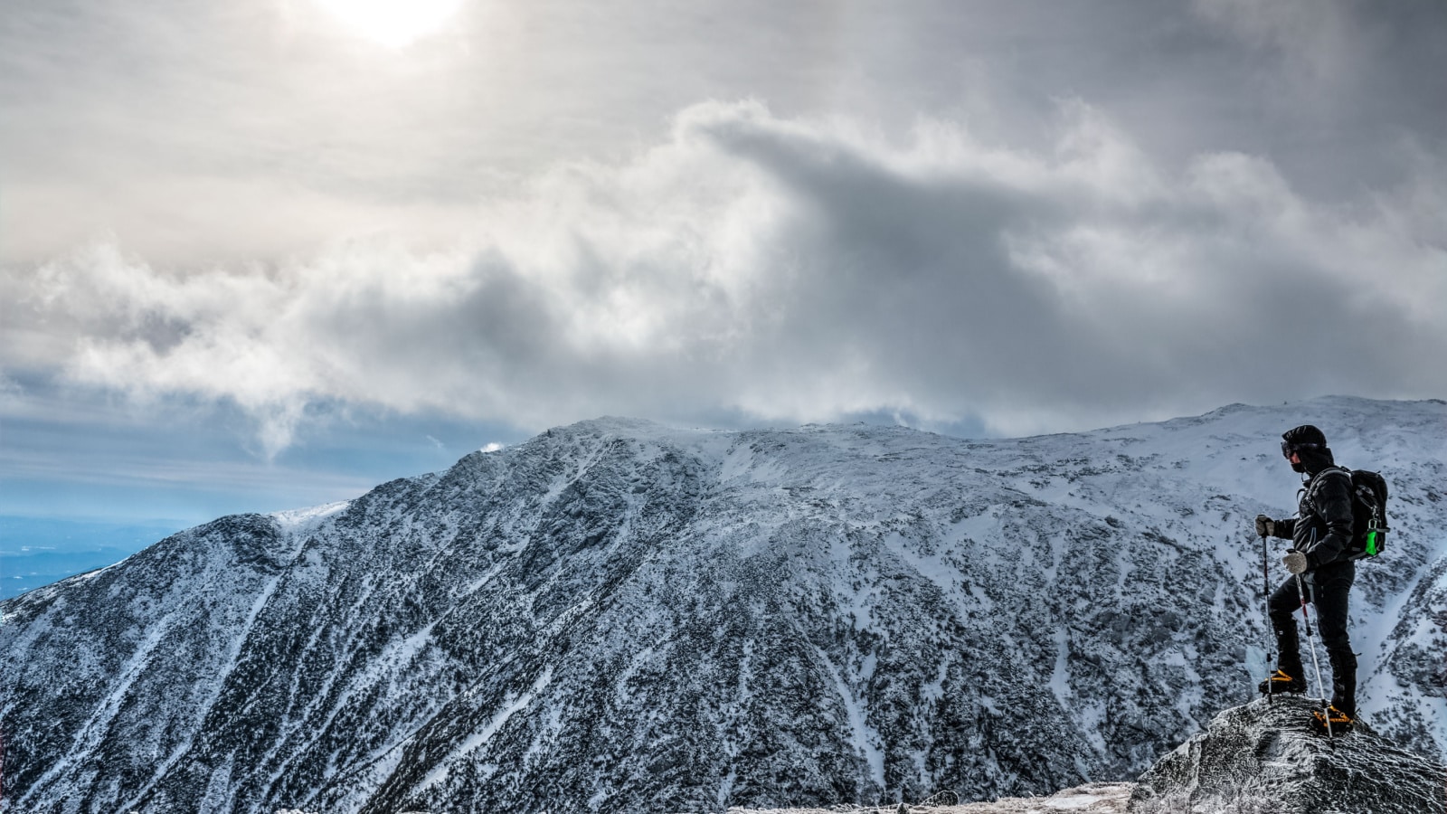 Man with equipement on the edge, hiking mount Washington in winter, looking over the ravine. New Hampshire, USA