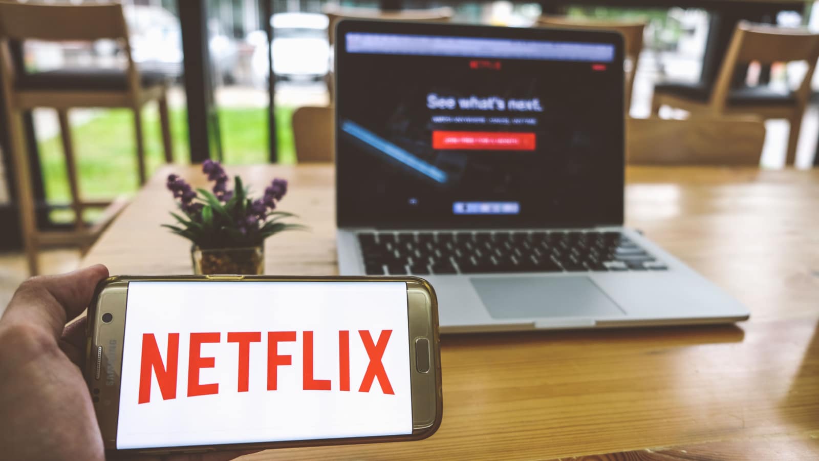 CHIANG MAI,THAILAND - July 28,2018: Man holds Mobile Phone using NETFLIX app on the screen with computer laptop on wooden table.