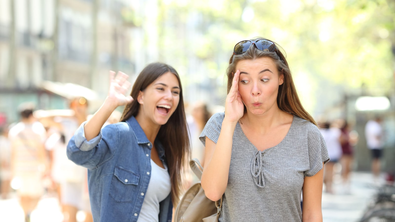 Happy teen greeting waving hand and friend ignoring her in the street