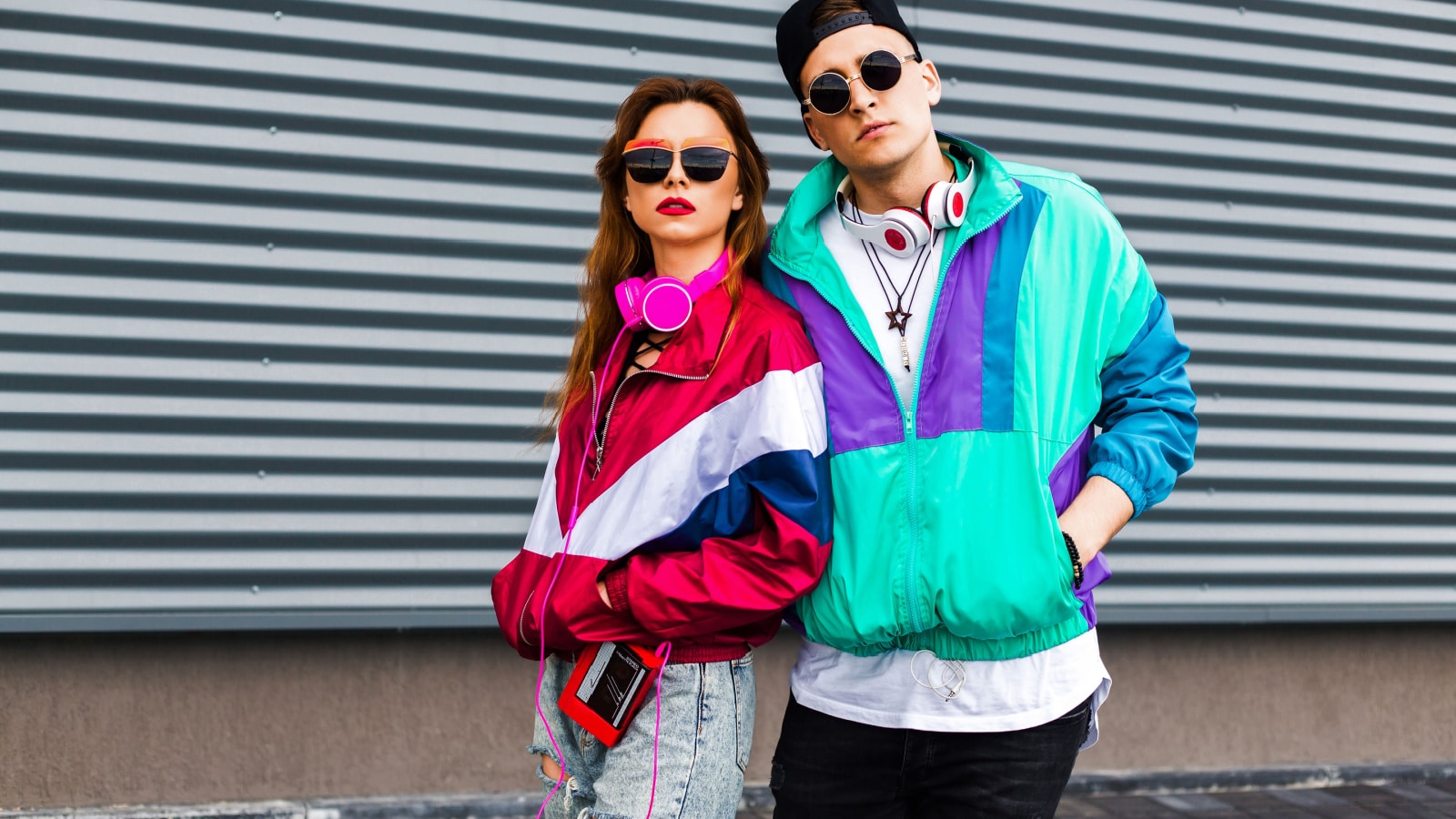 Back in time 90s 80s. Stylish young man in a retro jacket and a girl in red and with a vintage cassette player, against a steel wall, fashion trends, a street image