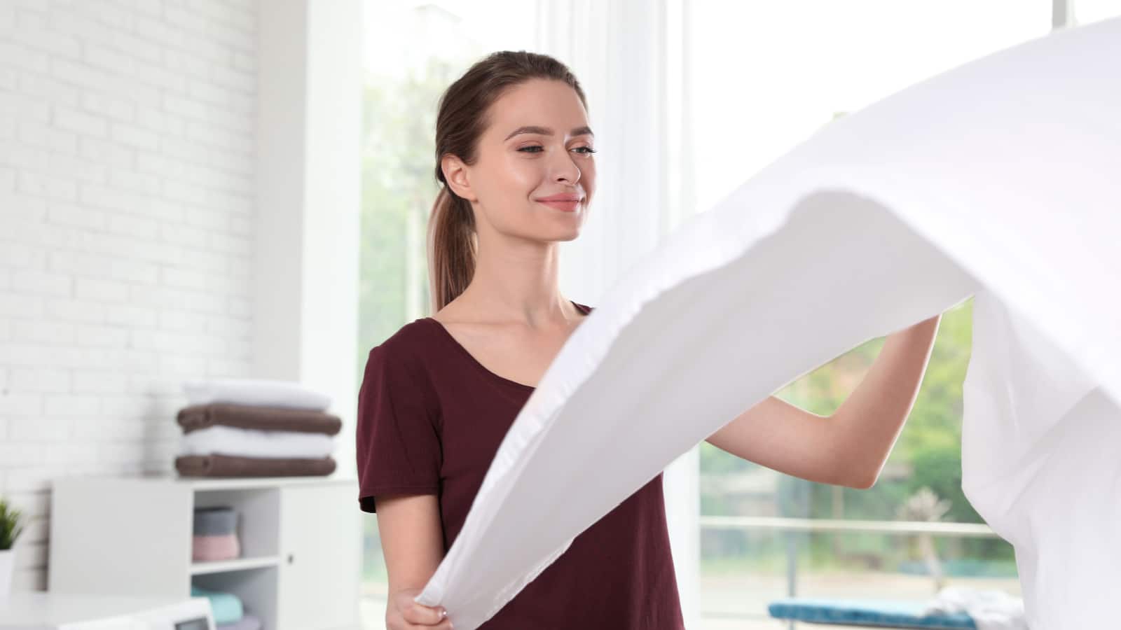 Young woman with clean bedsheet indoors. Laundry day