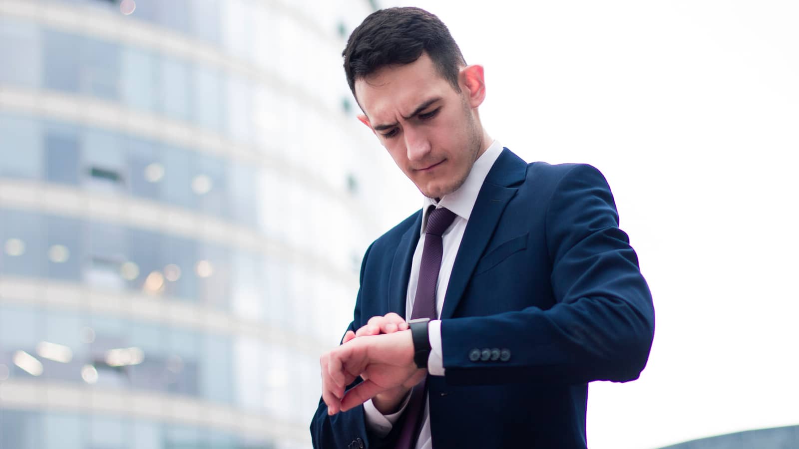Serious concentrated alarmed young businessman looking at his wrist watch, formal dressed guy in suit is late for a meeting. Distressed male rushing to meet, watching time. Business busy life concept.