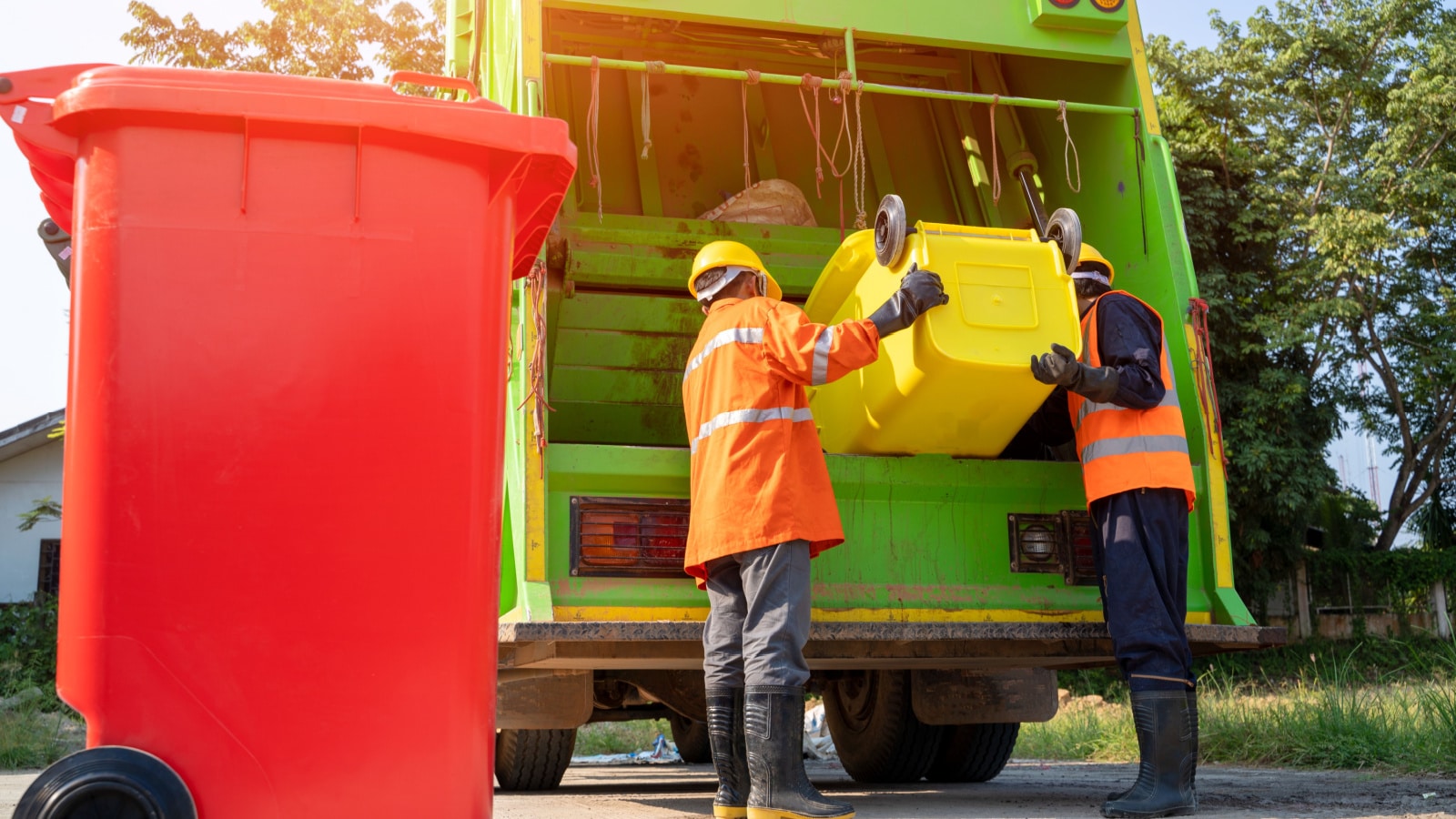 Two garbage men working together on emptying dustbins for trash removal with truck loading waste and trash bin.