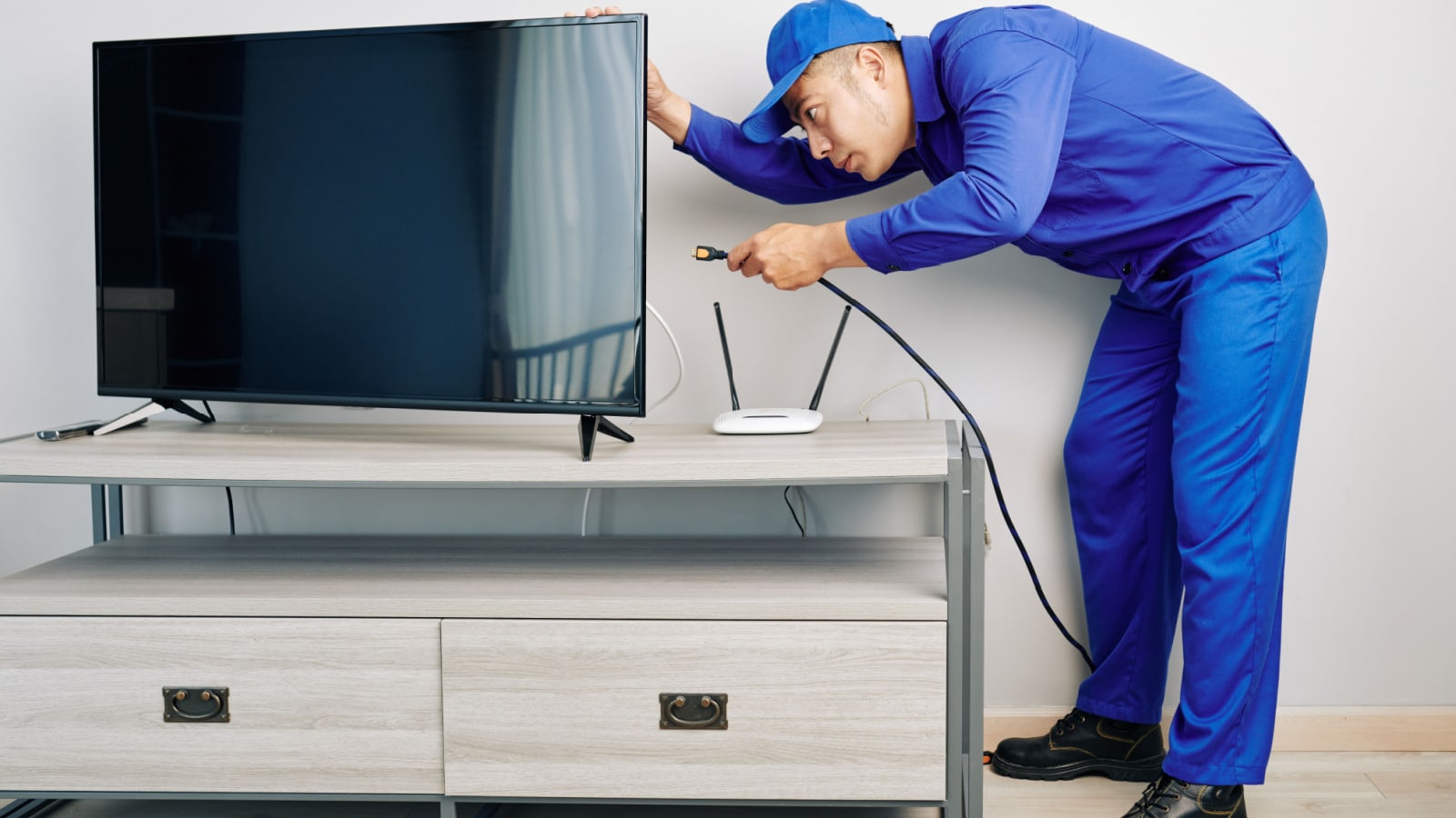 Serious young Vietnamese repairman installing tv set in apartment of customer