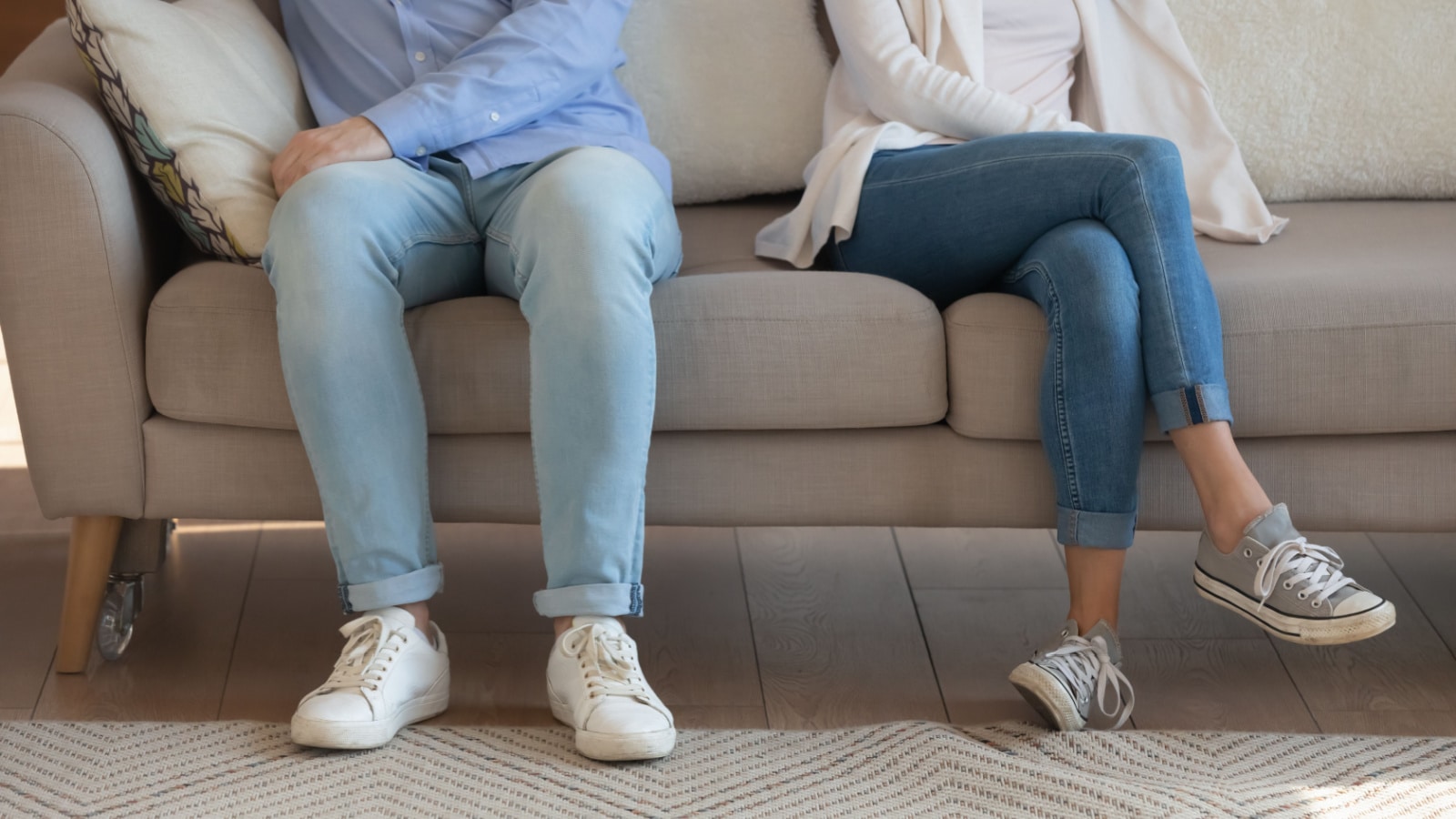 Close up legs view of unhappy upset young couple sit separately on sofa avoid talking after family fight, offended mad man and woman ignore, think of divorce or breakup, have relationship problems