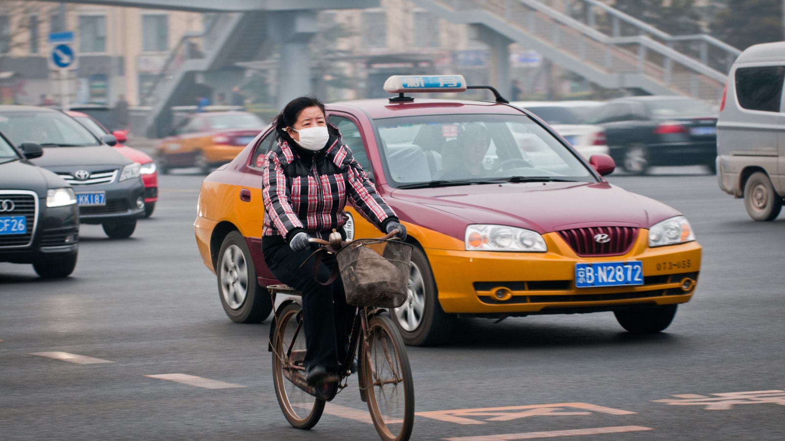 BEIJING, CHINA - MARCH 31: Woman with protective mask rides bike on a busy street in Dongcheng District on March 31, 2013 in Beijing