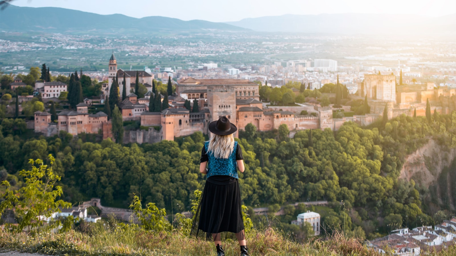 A young female traveler with sunglasses and casual style contemplates the views of the Alhambra palace in the city of Granada, Spain