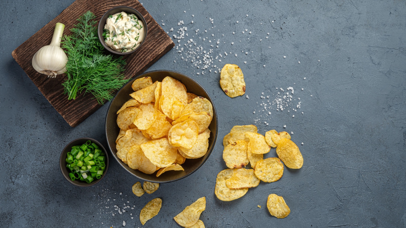 Potato chips on a dark gray background with ingredients. Top view, copy space.