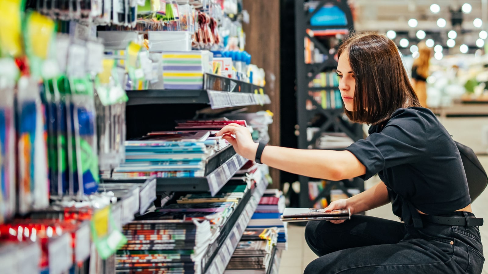 Portrait of young woman choosing school stationery in supermarket.