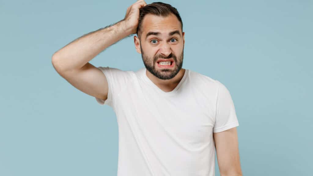 Young confused embarrassed sad puzzled man 20s wearing casual white t-shirt looking camera scratch head isolated on plain pastel light blue color background studio portrait. People lifestyle concept.