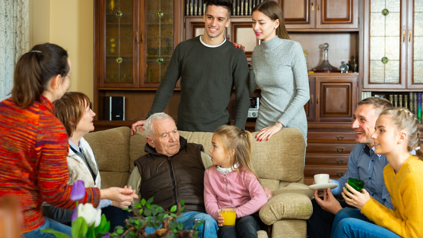 Happy large family gathered in parental home for family party, cheerfully talking in cozy living room