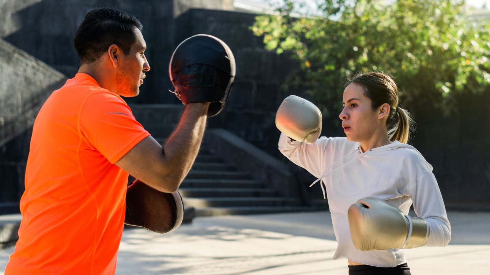 Boxing trainer teaching private lessons to a woman of Latino origin.