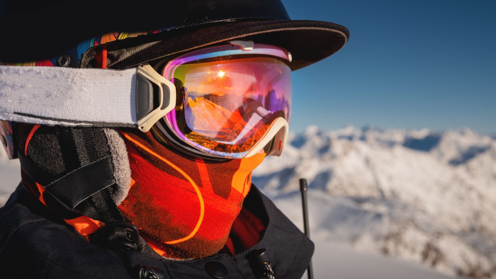 Profile of a female skier in ski goggles in the mountains. A woman in a sports ski jacket and snowboard sunglasses looks away. Sportswear and fashion for winter sports, ski resort