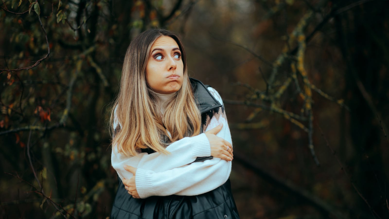Woman Wearing a Sweater and a Vest Feeling Cold. Lady feeling afraid and chill in the woods during autumn season