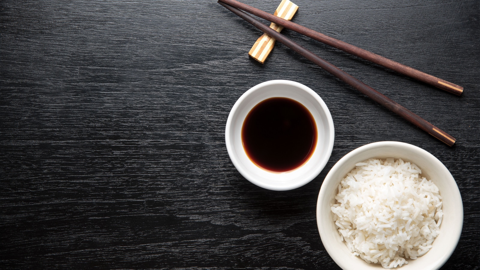 Japanese sushi chopsticks over soy sauce bowl, rice on black background. Top view with copy space