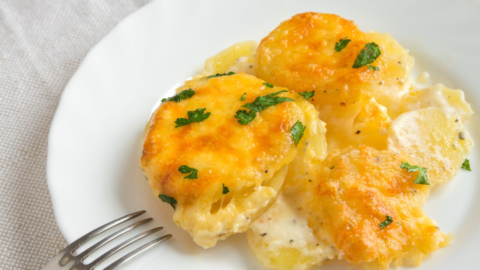 Potato gratin (casserole) with cream, cheese and parsley on white plate