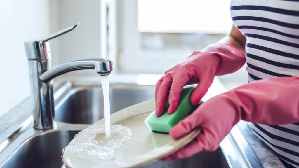 Cropped image of attractive young woman is washing dishes while doing cleaning at home